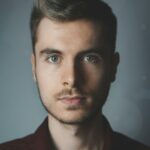 Close-up portrait of a young man with facial hair and a serious expression.